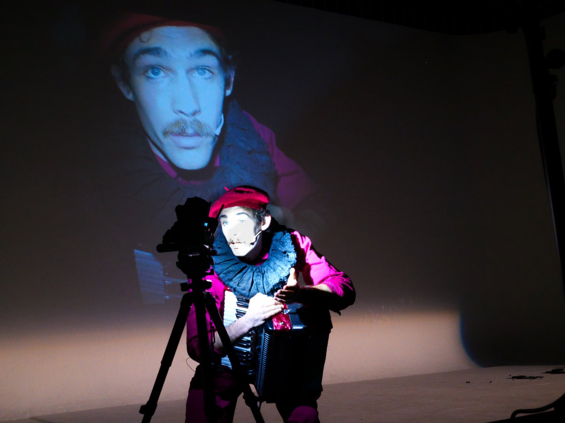 A performer with an accordion and camera, his face projected behind him at Volume 1